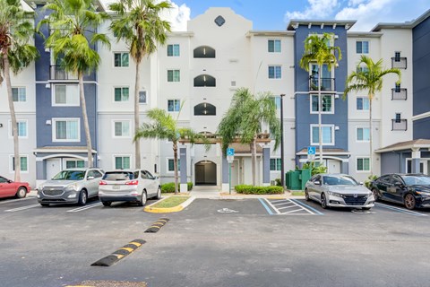 A parking lot in front of a multi-story building with cars parked.
