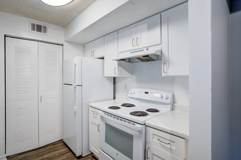 A white kitchen with a stove, refrigerator, and cabinets.