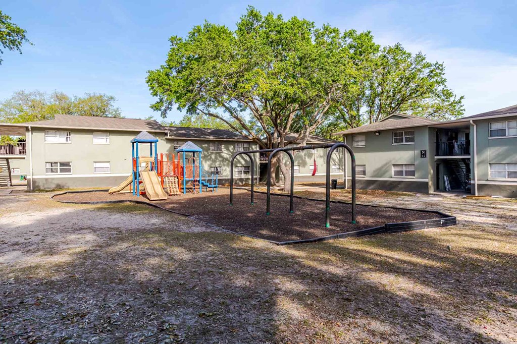 A playground with a swing set and a tree in the middle of a grassy area.