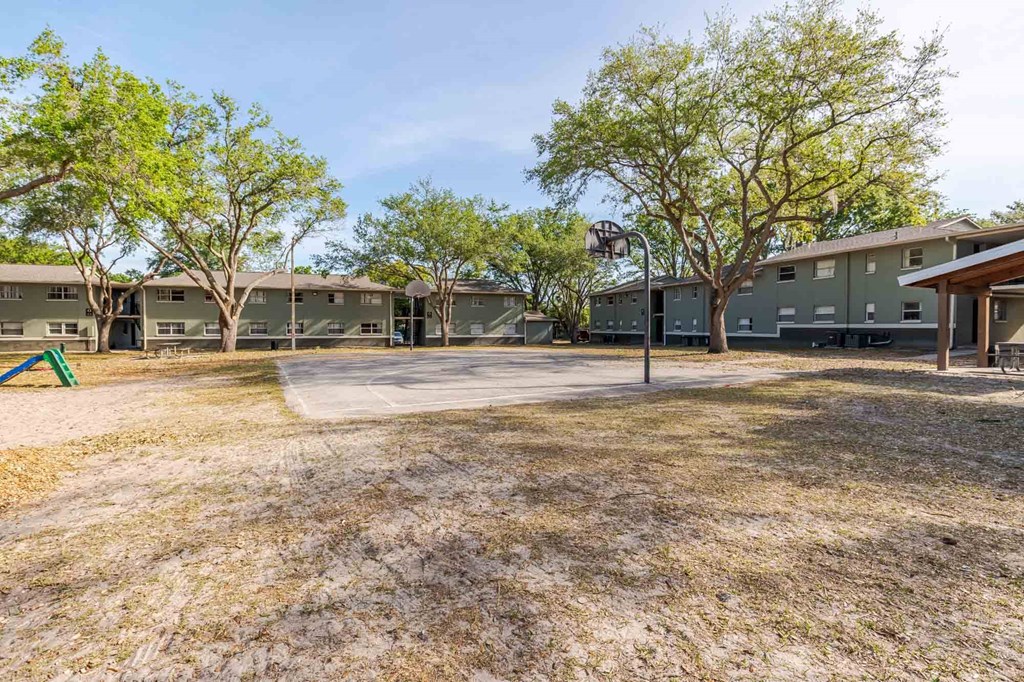 A playground with a basketball hoop and a green slide in front of apartment buildings.