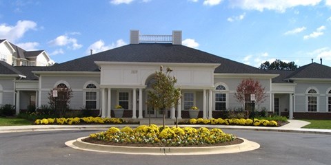 A large white house with a grey roof and a circular flower bed in front.