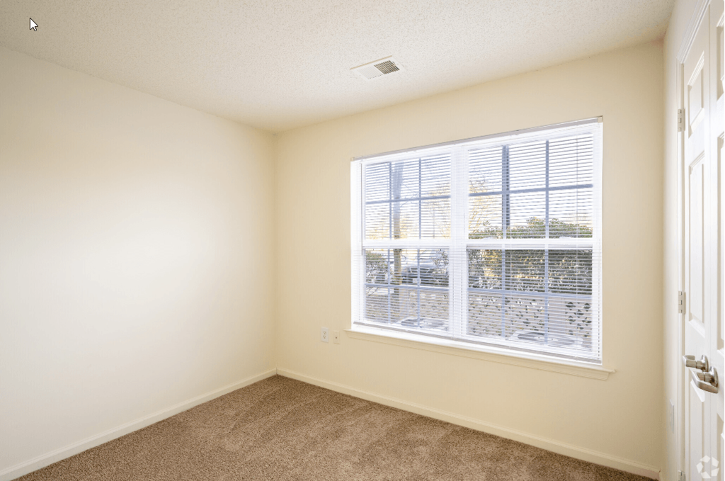 an empty bedroom with a large window and carpeted flooring