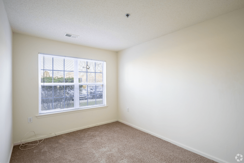 an empty room with a large window and carpeting