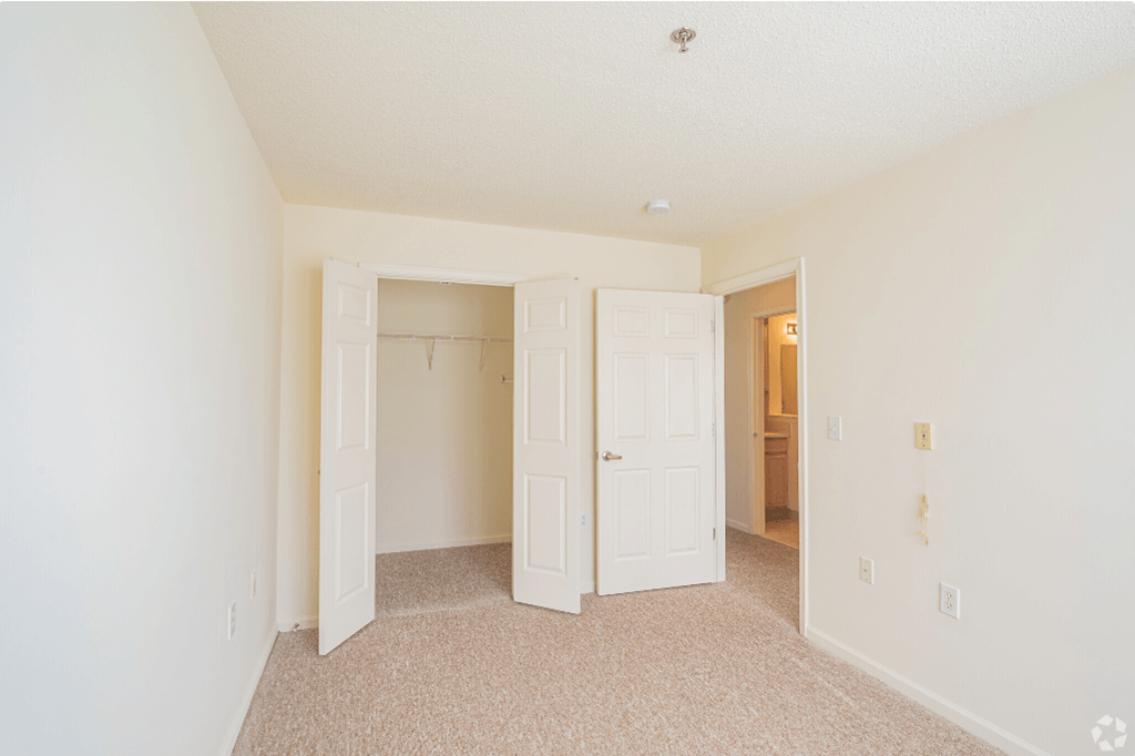 a bedroom with white doors and carpeting and a hallway to a closet
