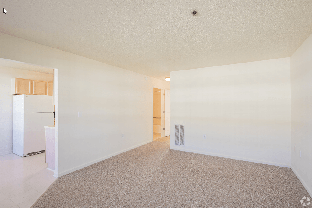 an empty living room and kitchen with a refrigerator and
