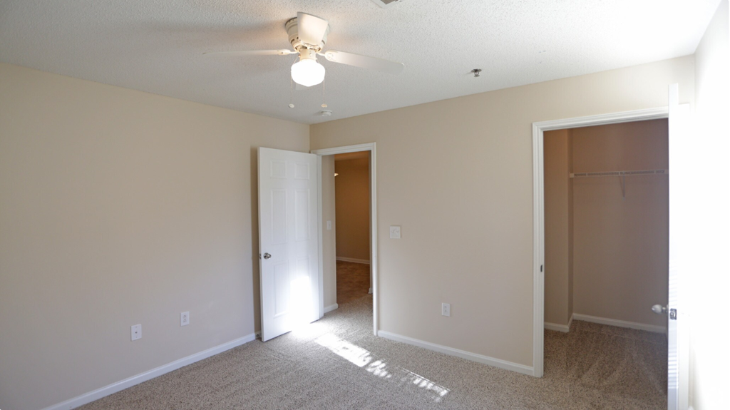 an empty living room with a ceiling fan and a closet