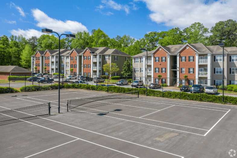 an empty tennis court with apartments in the background at Magnolia Lake Apartments, Georgia