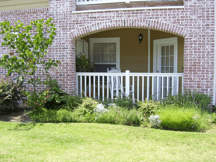 the front porch of a brick house with a white railing