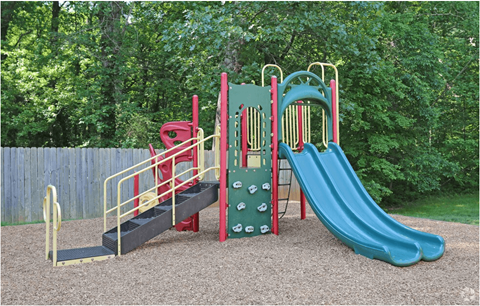 A playground with a green slide, red and yellow climbing frame, and a black ramp.