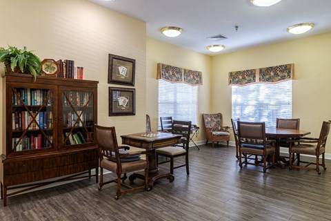 A room with a wooden floor, a bookcase, a table with chairs, and pictures on the wall.at The Gardens of Stafford, 22193