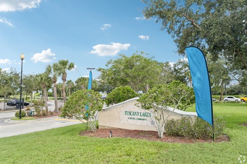A sign that says Tuscany Lakes is in front of a grassy area.
