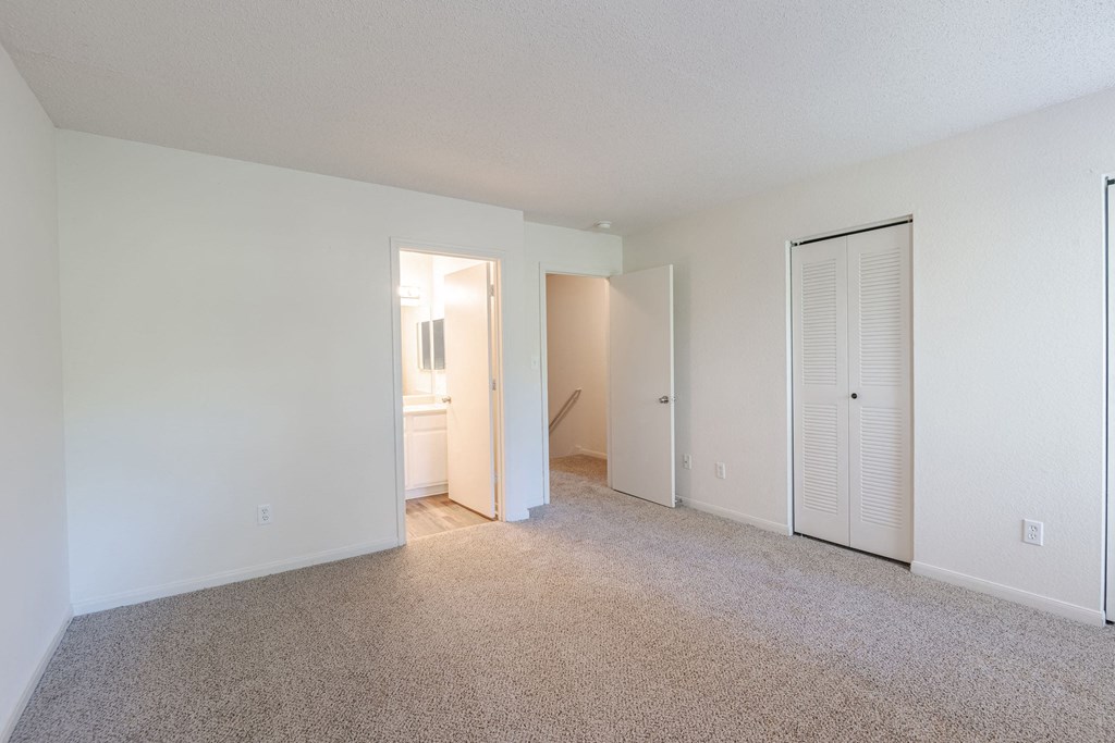 A sparsely furnished room with a carpeted floor and white walls.at The Village at England Run, Fredericksburg 