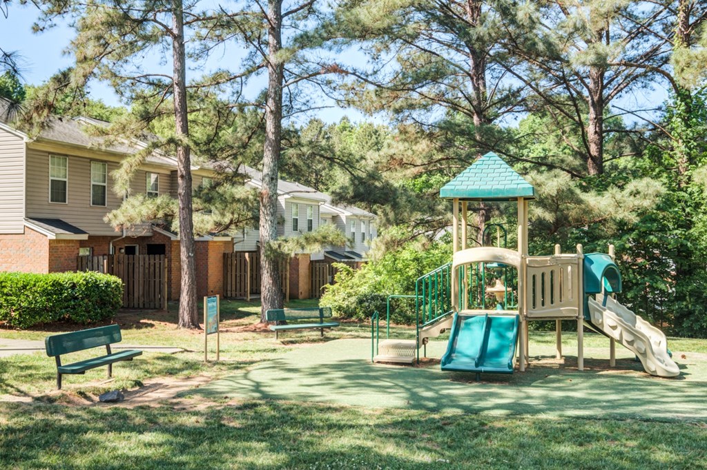 A playground with a green slide and a wooden swing set.