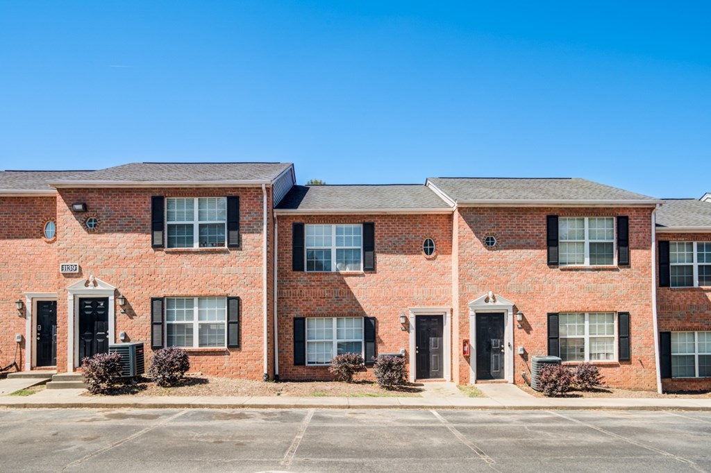 A row of red brick townhouses with black shutters and doors.