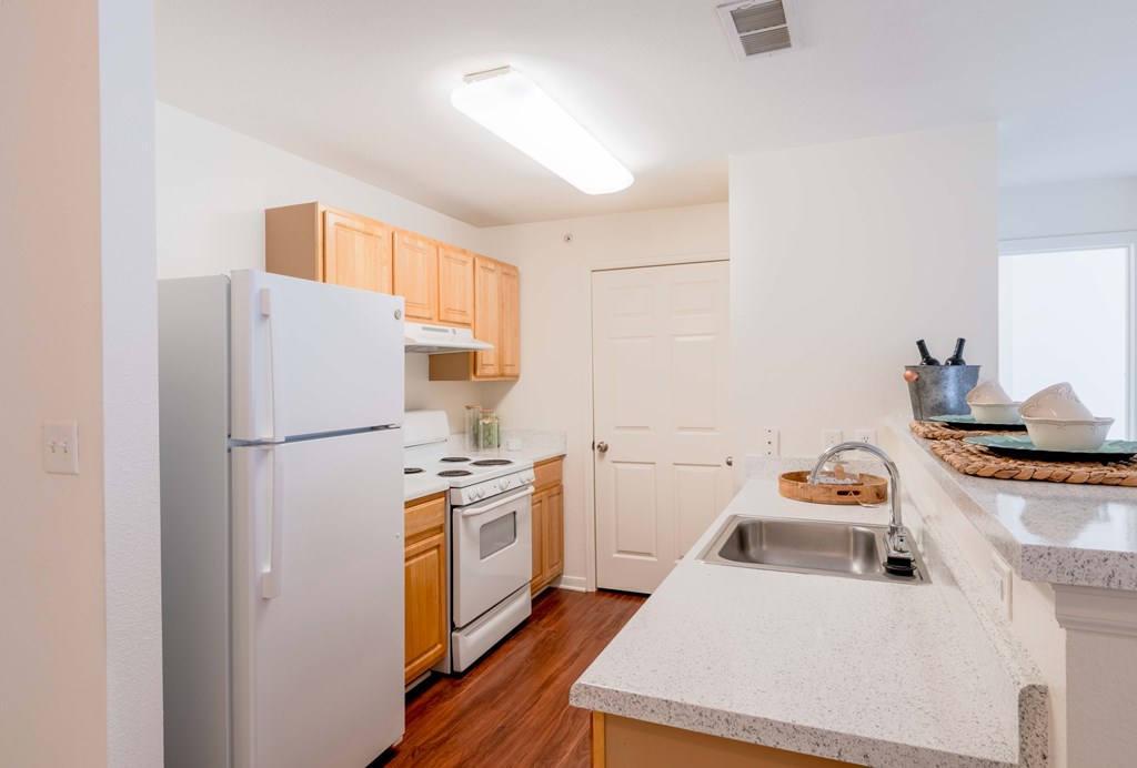 A kitchen with a white refrigerator, sink, and cabinets.
