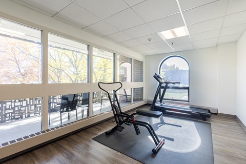 A gym room with a treadmill, exercise bike, and a chair.