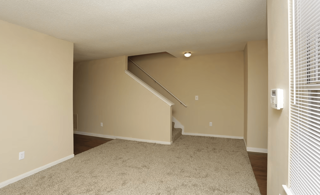 an empty living room with stairs and a carpeted floor