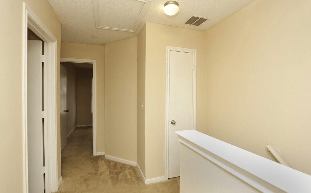 an empty hallway with white walls and a white railing and a door to a closet