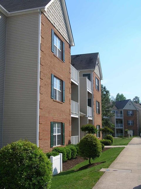 Apartment building with a white fence and green bushes in front.