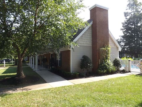 A small church with a red brick chimney is surrounded by a white picket fence and green trees.