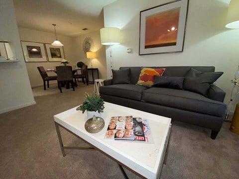 A living room with a grey couch, a white coffee table, and a painting on the wall.