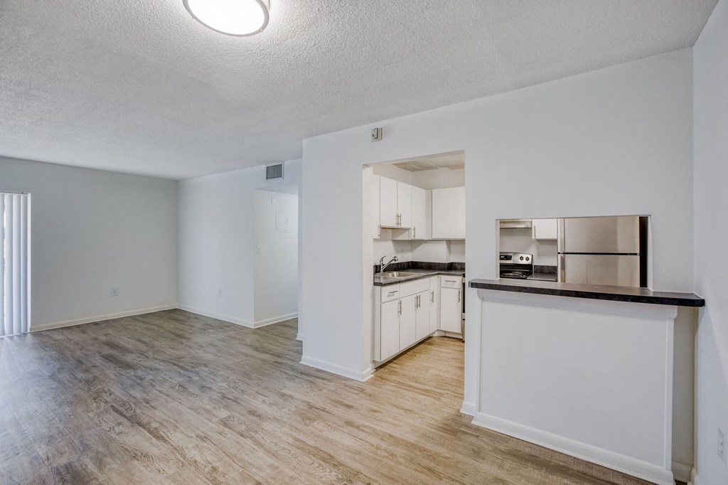 an empty living room with a kitchen in the background