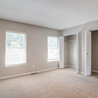 A room with a carpeted floor and two windows.