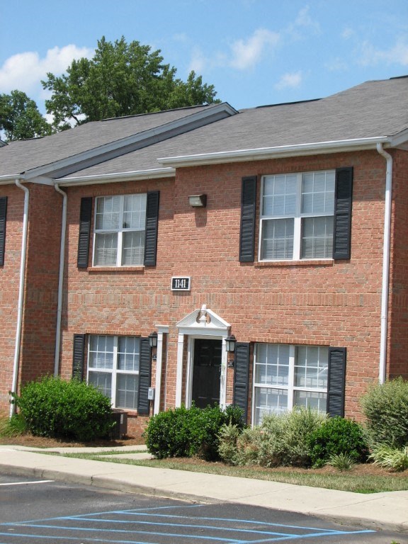 a brick house with black shutters and a sidewalk in front of it