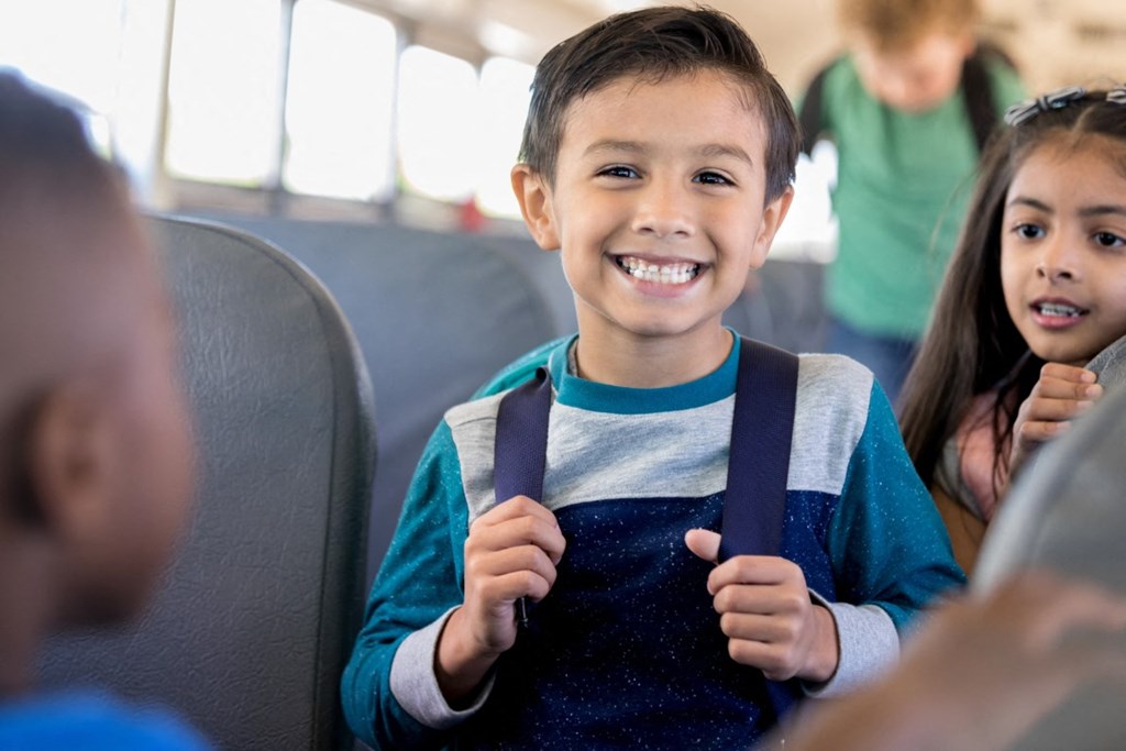 a young boy and girl sitting on a bus holding their school bags