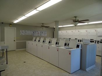 Bright laundromat with rows of open top-loading washing machines and tiled floors.