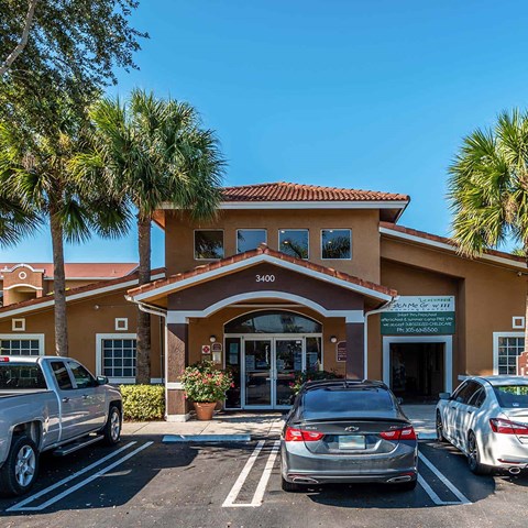 A building with a brown roof and tan walls with cars parked in front.
