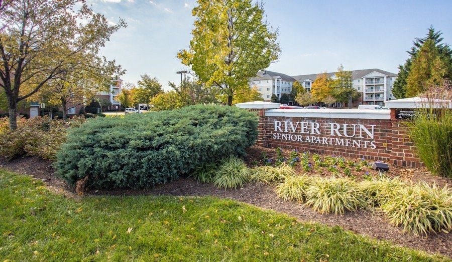 A sign for River Run Senior Apartments is surrounded by shrubbery.