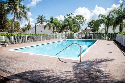 A small pool surrounded by a fence and palm trees.