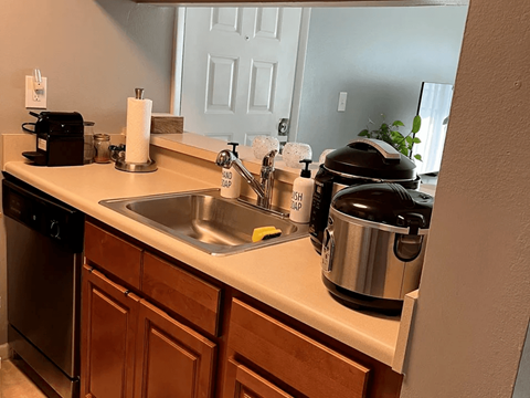 A kitchen with a stainless steel sink and a black pressure cooker on the counter.