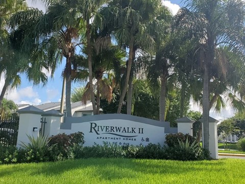 A sign for Riverwalk II Apartment Homes is in front of some palm trees.