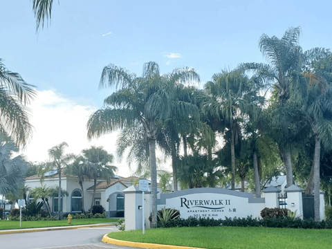 The image shows the entrance to Riverwalk II Apartments with a sign and palm trees.