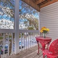 A red table with a vase of flowers on it sits on a porch.