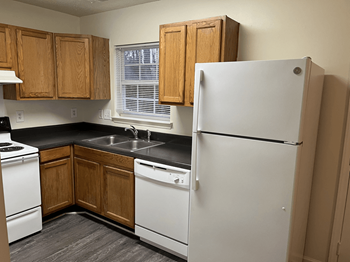 A white refrigerator stands in a kitchen with wooden cabinets and black countertops.