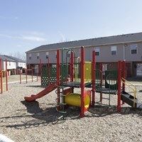 A playground with a red and yellow slide and a green and red swing set.
