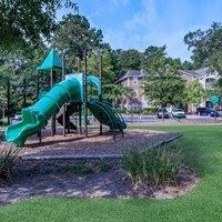 A green slide in a playground surrounded by trees.