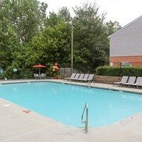 A pool with a diving board and lounge chairs.
