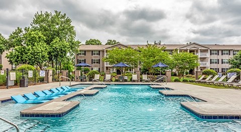 a swimming pool with chaise lounge chairs and umbrellas in front of an apartment building at The Bristol Apartments, Greenville, SC