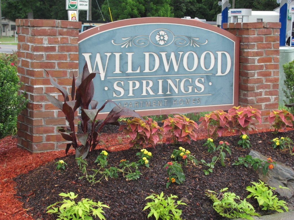 a sign for wildwood springs in front of a brick garden