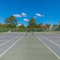 A tennis court with white lines and a clear blue sky in the background.