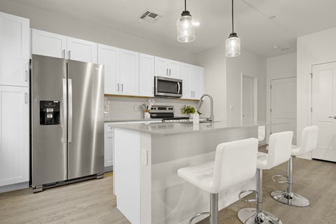 a kitchen with a large island with white chairs and a stainless steel refrigerator