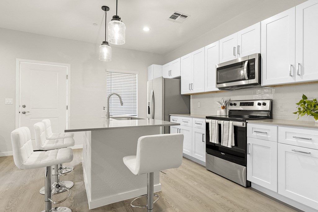 a kitchen with white cabinets and a bar with white chairs