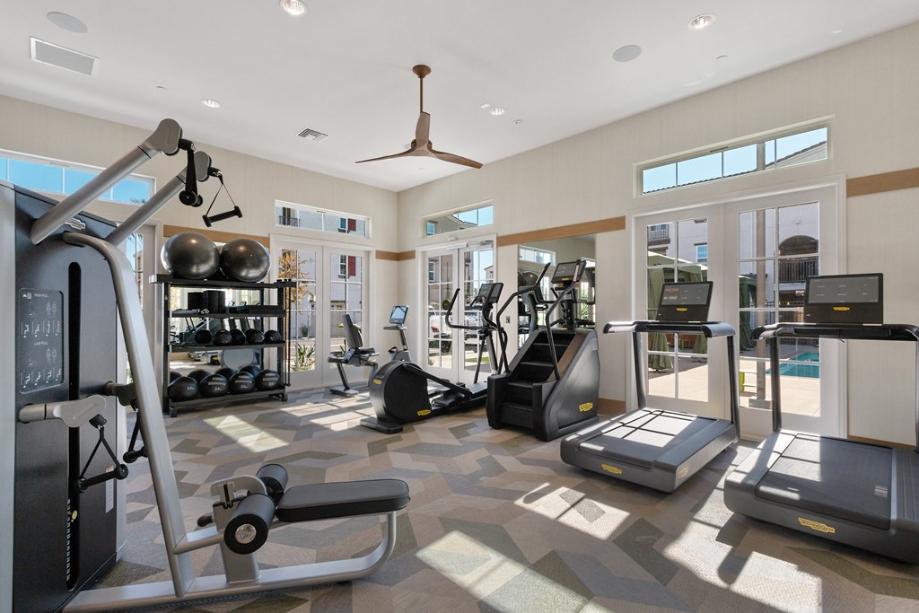 a gym with various machines and weights in a building with windows
