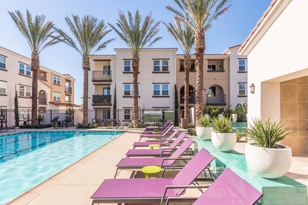 a swimming pool with pink lounge chairs and palm trees