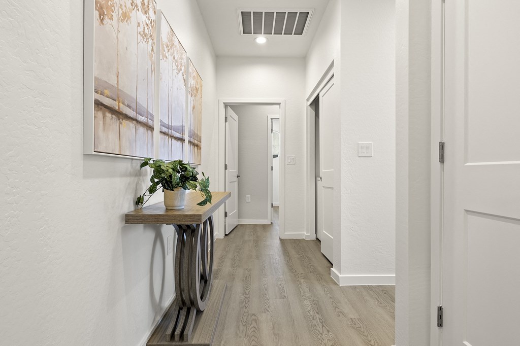 a long hallway with white walls and wood flooring and a table with a plant