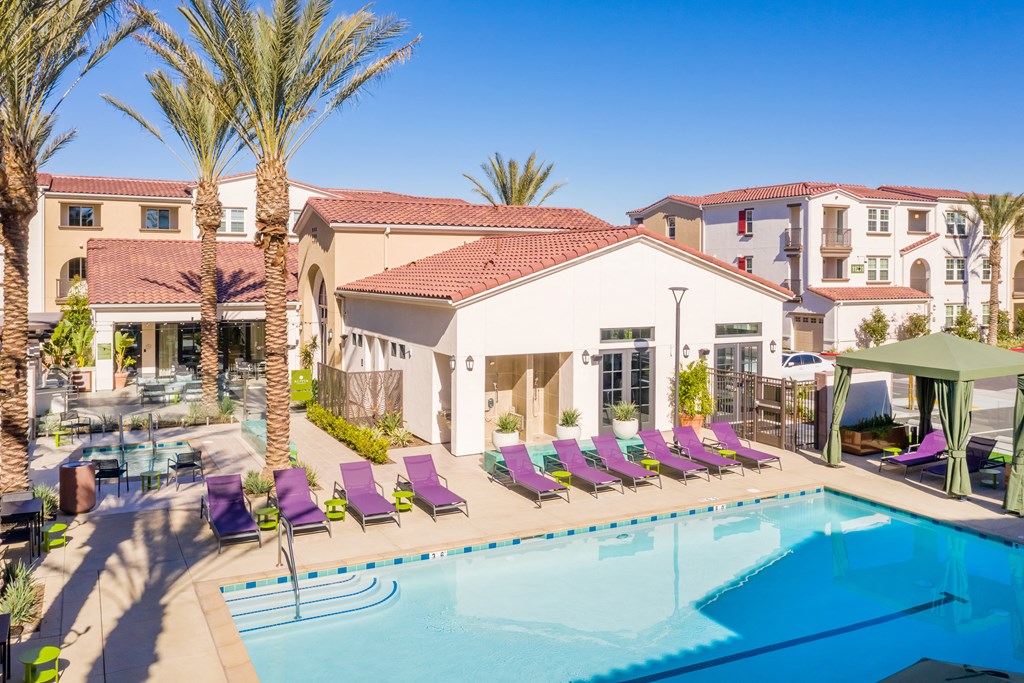 a swimming pool with purple lounge chairs around it and a house in the background